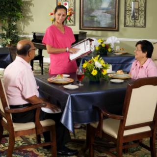 A waiter presenting a menu to two seated customers in a restaurant.