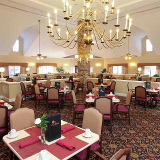 An elegant dining room featuring a grand chandelier and neatly arranged tables with red accents.