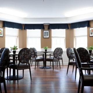 An empty dining area with multiple tables and chairs, featuring a wooden floor and small plants on the tables.