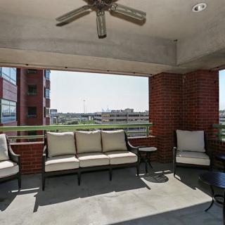 A spacious outdoor balcony with comfortable seating and a ceiling fan, surrounded by brick walls.