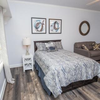 A cozy bedroom featuring a bed with patterned bedding, a sofa, wood flooring, and decorative elements.