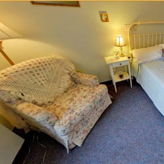 A cozy bedroom featuring a comfortable armchair, bedside table with a lamp, and a neatly made bed.