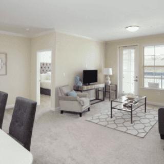 A modern living room in an apartment with neutral tones, featuring a sofa, TV, and coffee table.