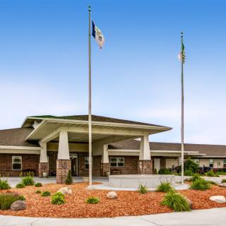 A building entrance with landscaped surroundings and flags on poles under a clear blue sky.