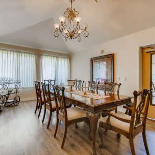 A spacious dining room featuring a large wooden table, multiple chairs, a chandelier, and natural light from tall windows.