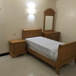 A minimalistic bedroom with a single wooden bed, nightstand, and dresser with mirror.