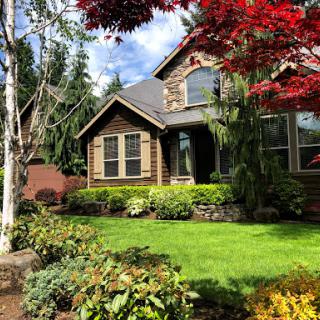 A charming house surrounded by a vibrant garden with lush greenery and colorful foliage.