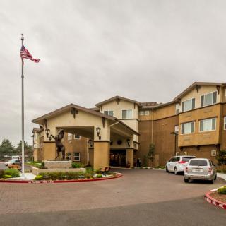 Entrance of a hotel with an American flag and parked cars under an overcast sky.