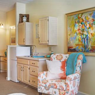 A cozy living space featuring a kitchenette, an armchair with floral patterns, and a vibrant abstract painting on the wall.