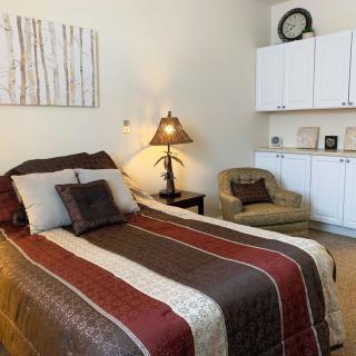 A cozy bedroom with a striped bedspread, an armchair, and a lamp beside the bed.