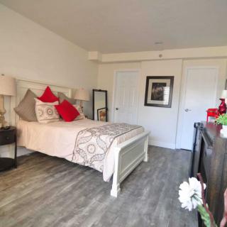 A cozy bedroom with a neatly made bed adorned with red and beige pillows, a bedside table with a lamp, and decorative elements enhancing the warm ambiance.