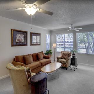 A cozy living room with a sofa, armchairs, and a coffee table illuminated by natural light through large windows.