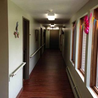 A long, well-lit hallway with wooden flooring and windows adorned with colorful decorations.