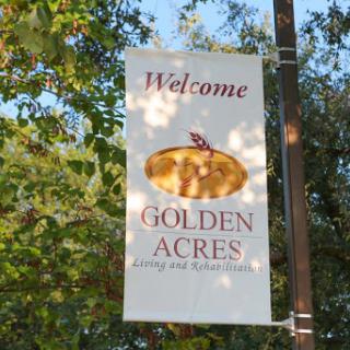 A welcome sign for Golden Acres, surrounded by greenery.