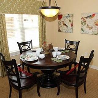 A cozy dining room with a round table set for four, featuring elegant chairs and decorative artwork on the walls.