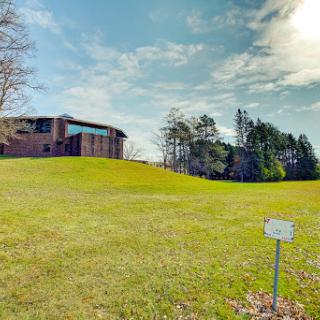 A modern building set against a lush green landscape under a partly cloudy sky.