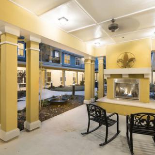 A cozy outdoor patio with rocking chairs and a fireplace, sheltered by a covered ceiling supported by columns.