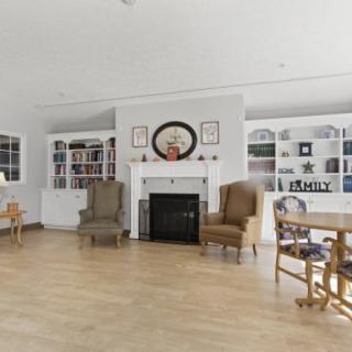 A cozy living room with a fireplace, surrounded by armchairs and built-in bookcases on a wooden floor.