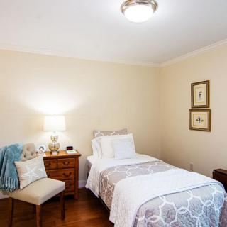 A cozy bedroom with a single bed, nightstand, lamp, and a chair.