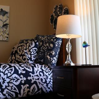 A cozy bedroom setup featuring patterned bedding and a stylish lamp on a dark wooden nightstand.
