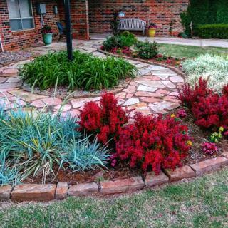 A beautifully landscaped garden featuring vibrant red plants and a stone pathway.