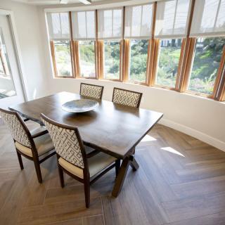 A bright dining area with a wooden table and chairs surrounded by large windows.