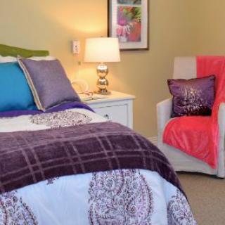 A cozy bedroom setup with colorful pillows and a comfortable chair.