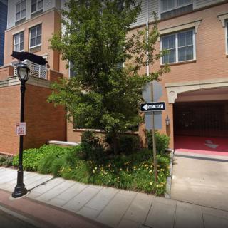 A street view of a brick apartment building with greenery and a lamp post.