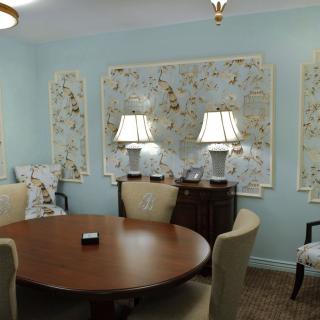 A cozy room with a round wooden table, surrounded by upholstered chairs and adorned with decorative artwork and lamps.
