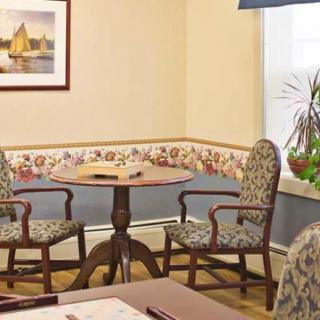 A cozy corner with a small table and two upholstered chairs next to a window, decorated with a painting and houseplant.