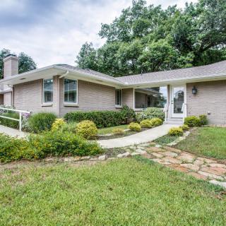 A ranch-style house with a neatly maintained front yard and pathway surrounded by greenery.