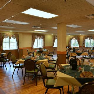 A spacious dining room with neatly arranged tables and chairs, featuring natural lighting and decorative curtains.