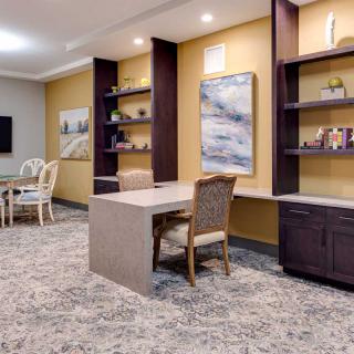 A modern office space with a large desk, built-in shelves, and a meeting area in the background.