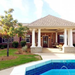 A brick house with a porch and swimming pool in the foreground.