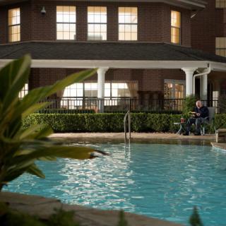 A serene outdoor pool area in front of a building at dusk with a person sitting nearby.