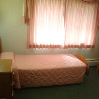 A cozy bedroom featuring a single pink bed and soft curtains that let in natural light.