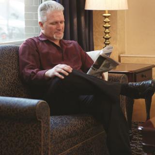A person relaxing in a chair while reading a newspaper indoors.