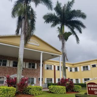 A charming residential building surrounded by lush greenery and palm trees under a cloudy sky.