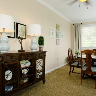 A cozy dining room with a wooden table and chairs, complemented by a sideboard adorned with decorative lamps and wall art.