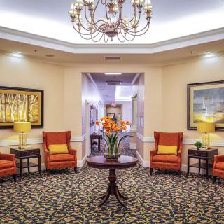 A well-decorated lobby featuring a central table with flowers, surrounded by comfortable chairs and illuminated by a chandelier.