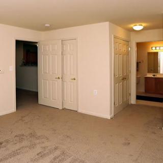 An empty bedroom with carpet flooring, featuring closets and a doorway leading to a bathroom.