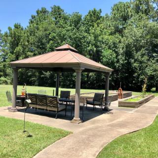 A relaxing outdoor gazebo with patio furniture, surrounded by a lush lawn and trees.