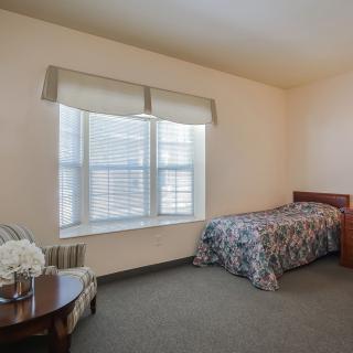 A minimalist bedroom with a single bed, window, and table with flowers.