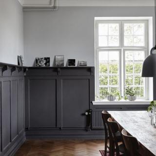 A minimalist dining room with dark furniture and natural light streaming through a large window.