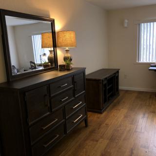 A well-decorated bedroom corner featuring a dresser with a mirror and a lamp, set on hardwood flooring.