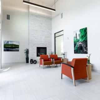 A modern, minimalist living room featuring white walls, a fireplace, and orange armchairs complemented by vibrant artwork.