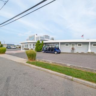 A small building next to a parking lot with golf carts parked outside, adjacent to a road under a clear sky.