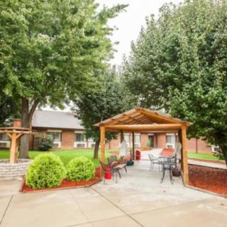 A cozy outdoor gazebo surrounded by trees and landscaping, featuring benches and a paved patio.