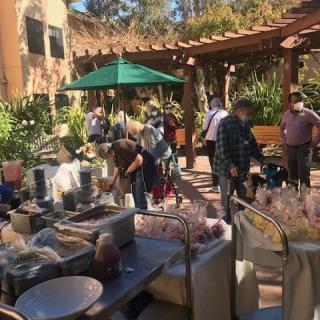 People browsing items at an outdoor market in a garden setting.