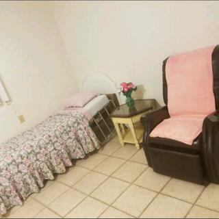 A cozy bedroom setup featuring a bed, a recliner chair, and a small table with flowers.